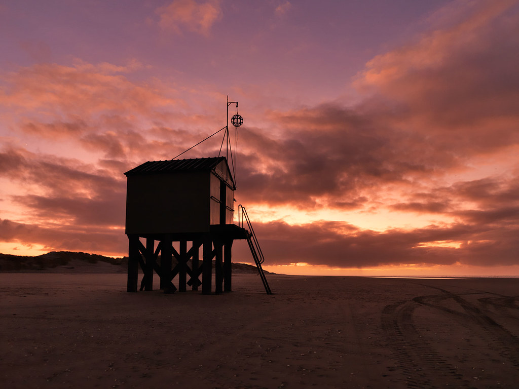 Beach hut on stilts beneath a vivid red evening sky