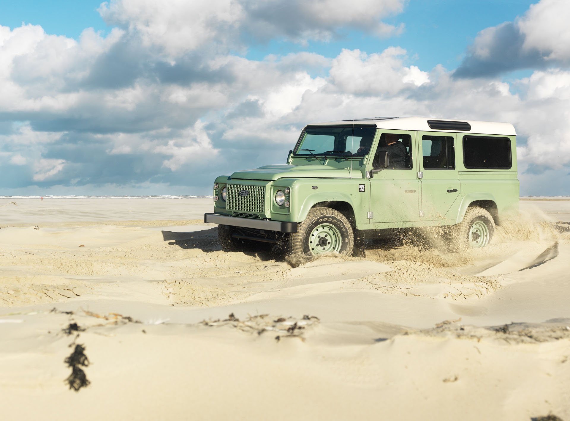 Green off-road vehicle driving through beach sand