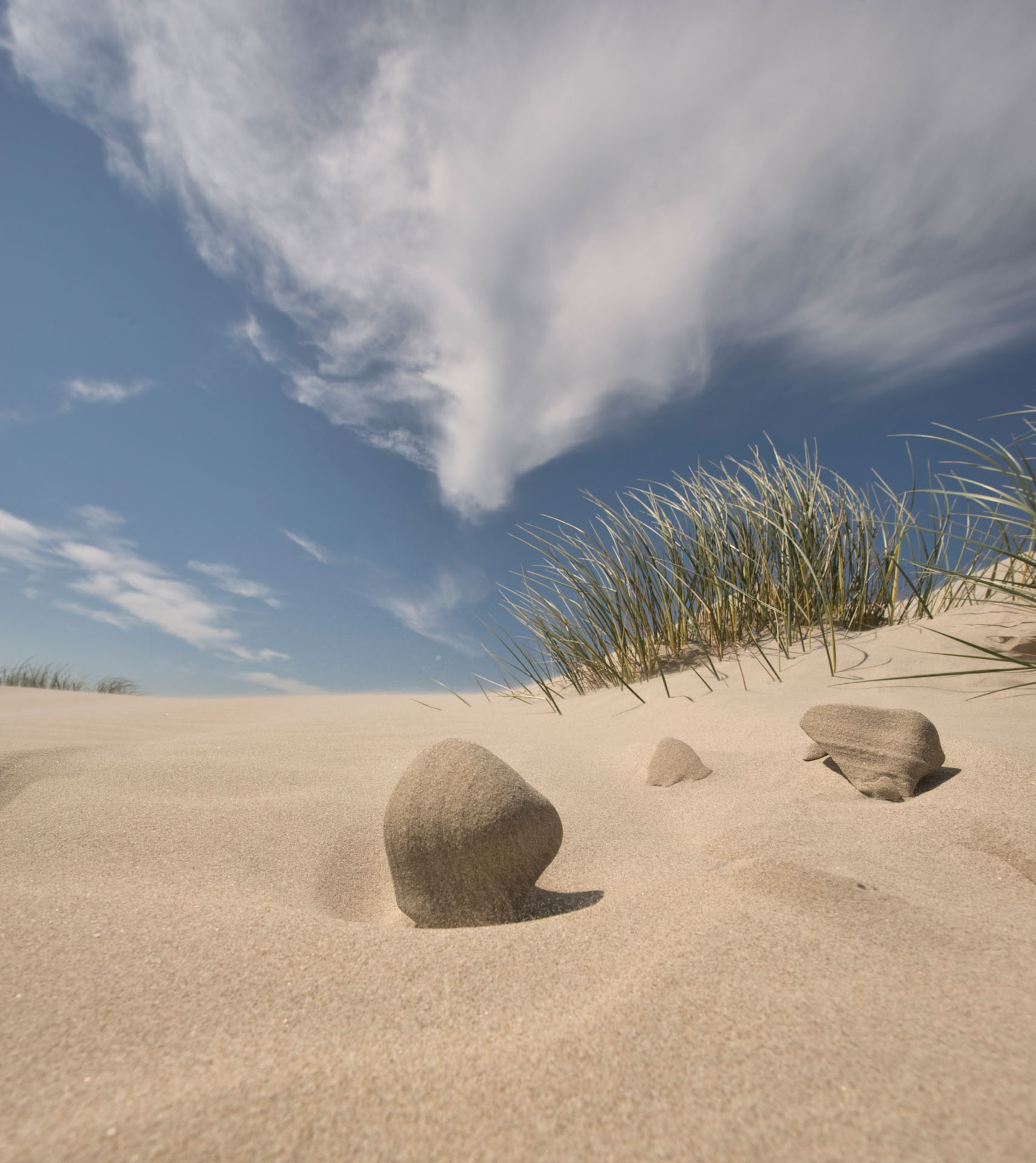 Rounded sand formations beneath dune grass and clouds