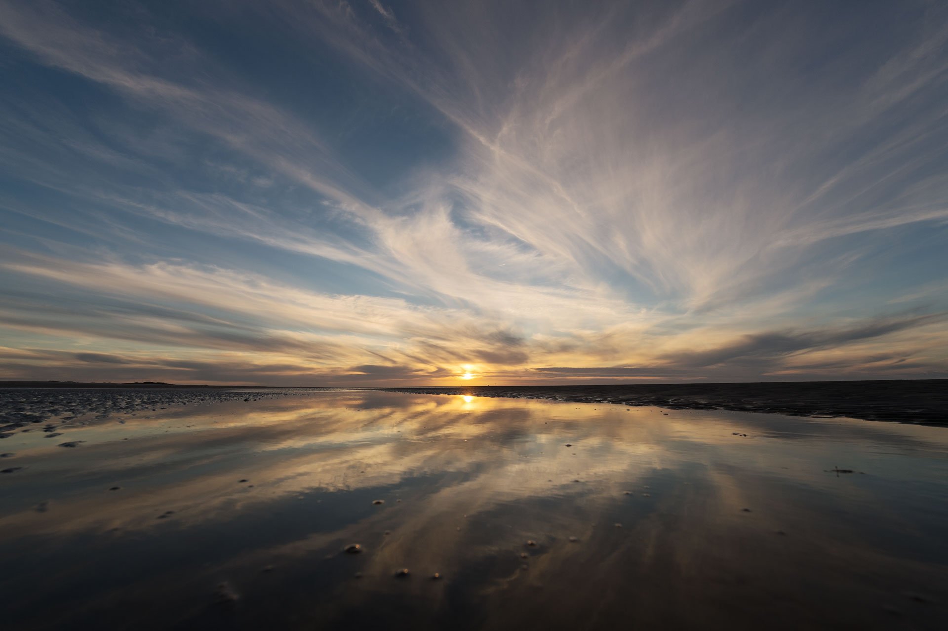 Wispy clouds and sunset reflected across the beach